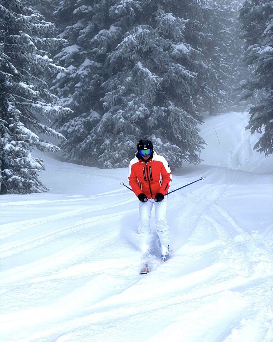 Skifahrer in roter Jacke auf einer verschneiten Piste zwischen Bäumen