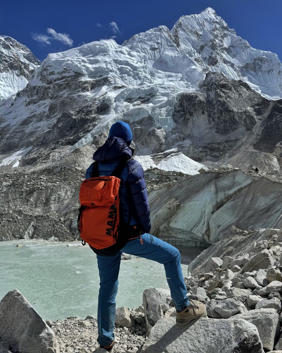 Trekker mit rotem Rucksack vor einer verschneiten Himalaya-Wand